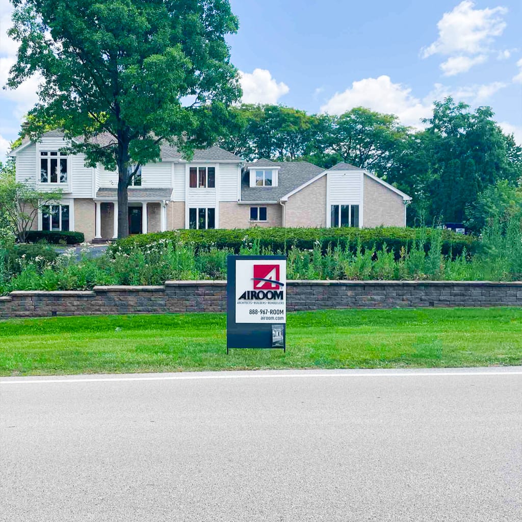 Two-story home with Airoom sign, green lawn, and trees.